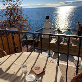 Restaurant am Meer, Tasse mit Kaffe und Glas Wasser steht am Tisch im Restaurant. Shoptimizer aus Holz
